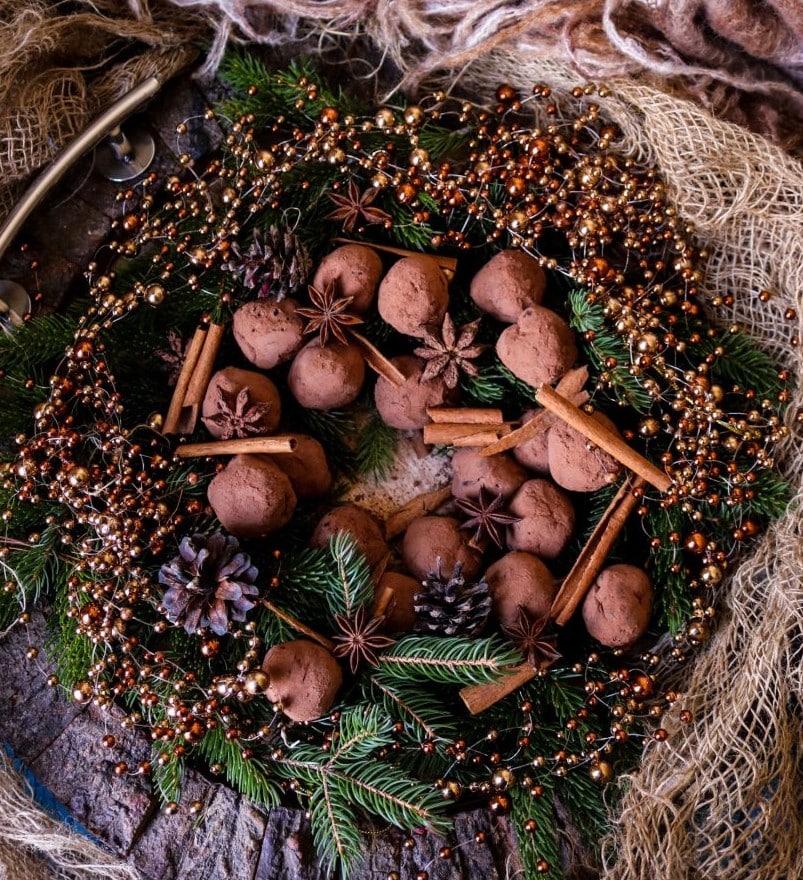 Gingerbread chocolate truffles arranged on evergreen branches with spices and a glowing candle in the centre.