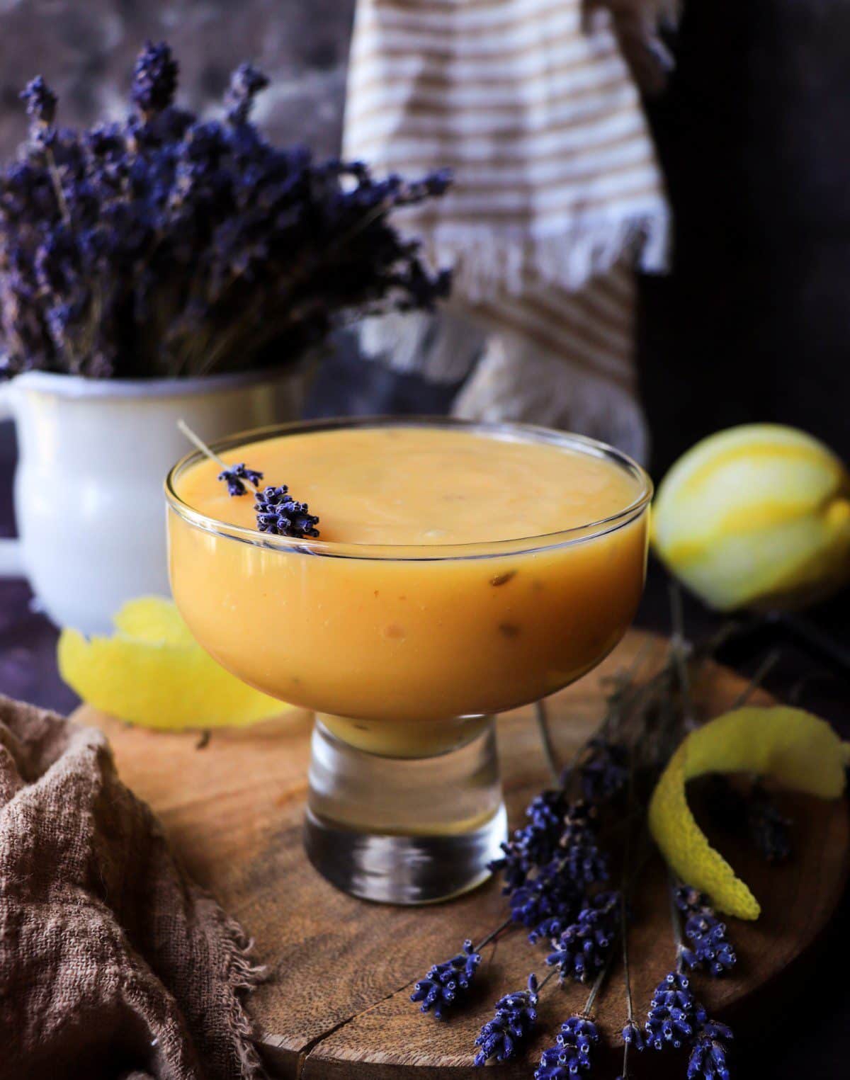 Lavender Lemon Curd in a glass dessert bowl garnished with dried lavender, fresh lemon peel, and lavender sprigs on a wooden board.