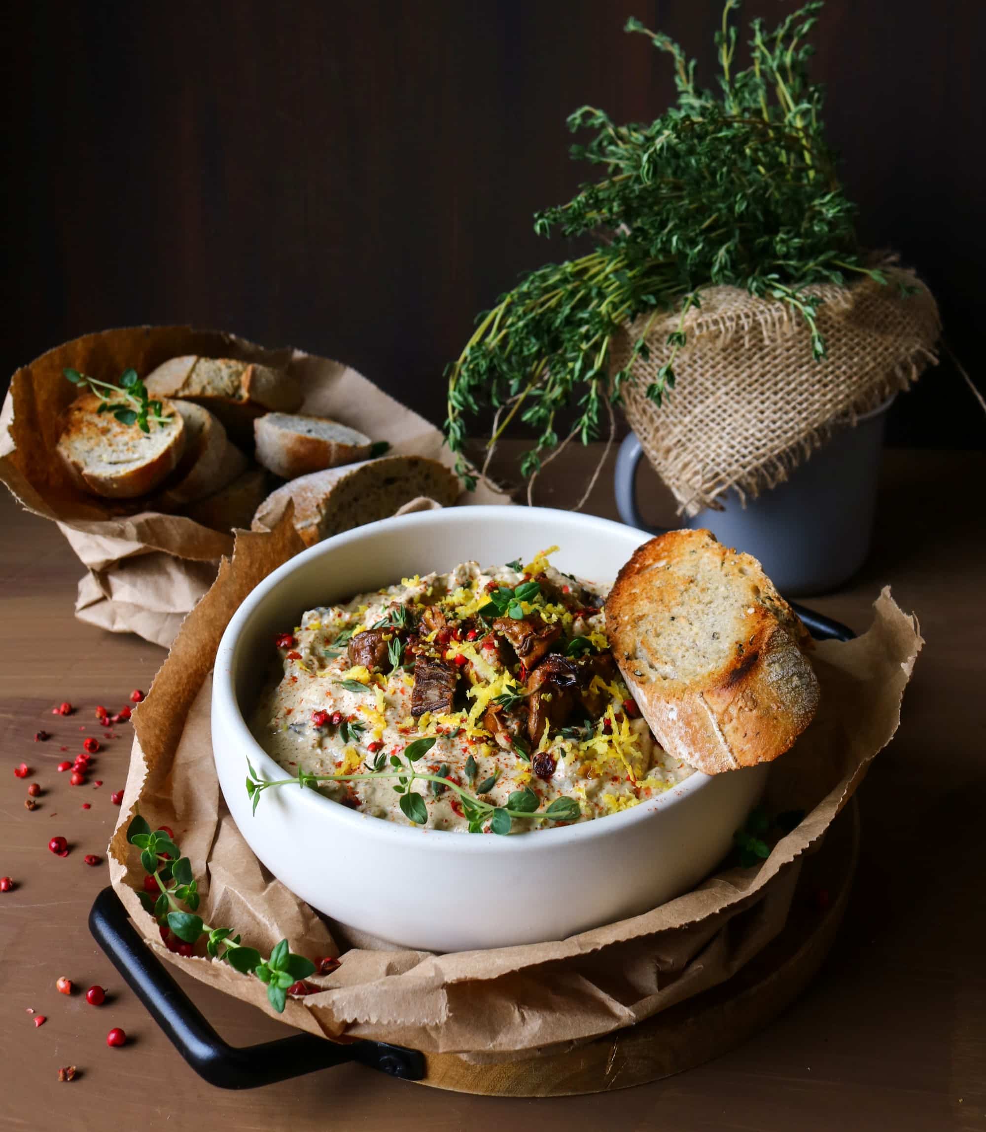 Smoked Oyster Spread in a white bowl topped with chopped smoked oysters, lemon zest, thyme, and pink peppercorns, served with toasted rustic bread.