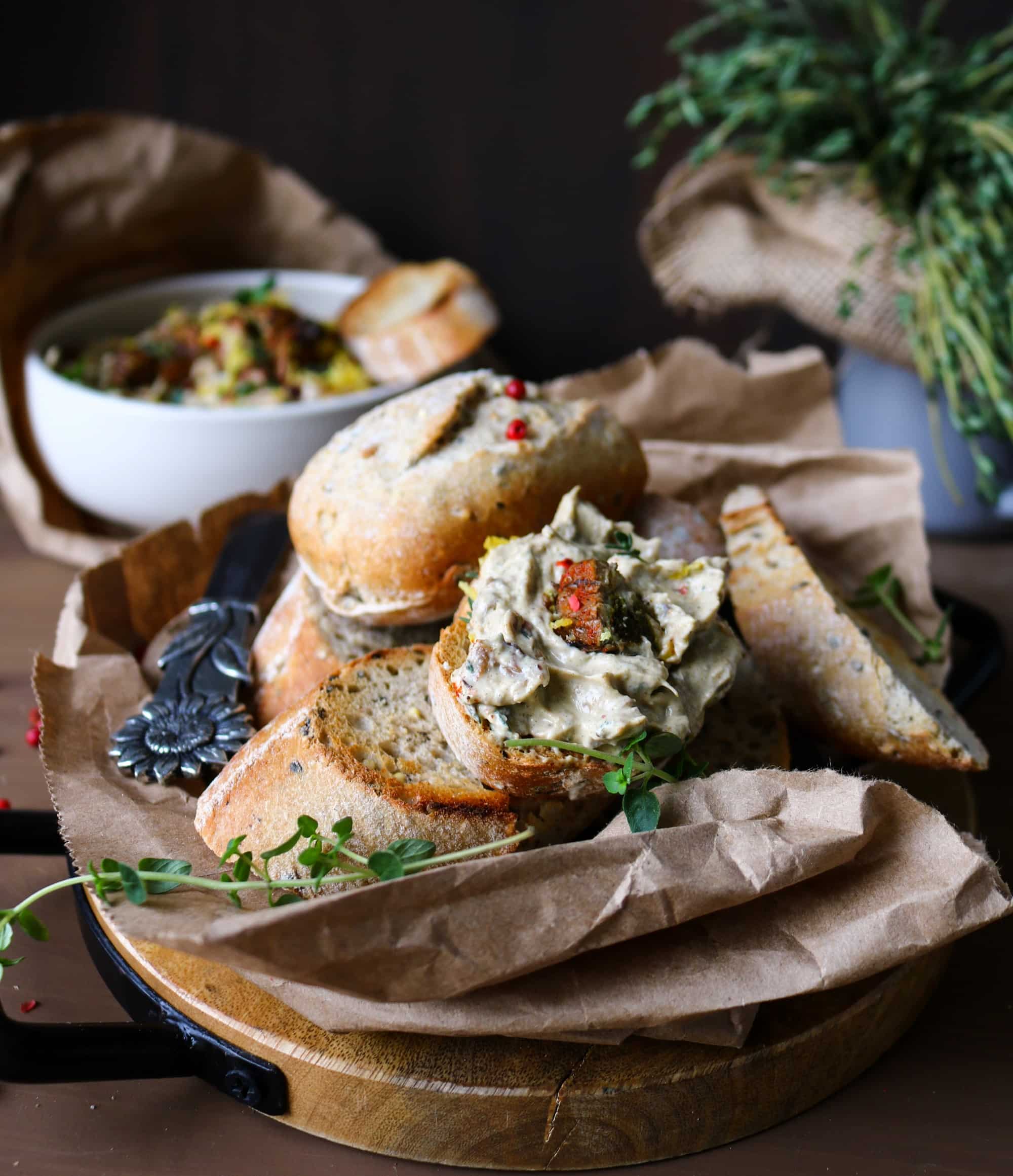 Toasted rustic bread topped with creamy Smoked Oyster Spread and garnished with thyme and pink peppercorns, with the spread bowl in the background.
