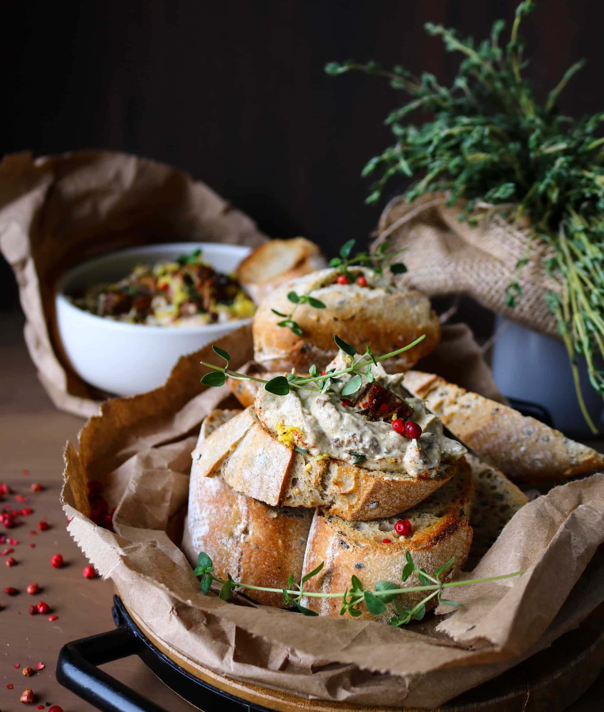 Toasted rustic bread topped with creamy Smoked Oyster Spread and garnished with thyme and pink peppercorns, with the spread bowl in the background.