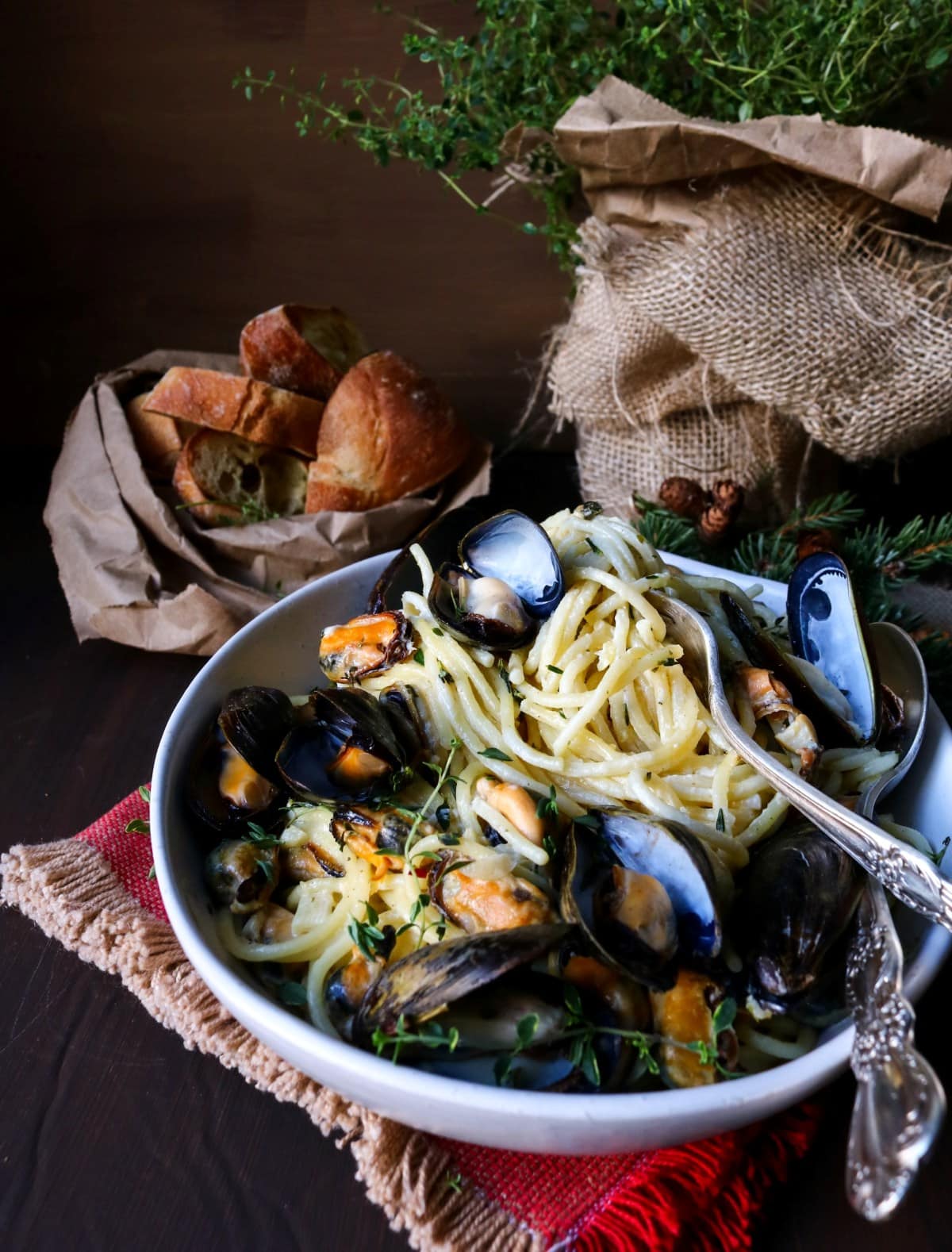 Garlic butter mussel pasta served in a white bowl with spaghetti, fresh thyme, and toasted bread on a dark wooden table.