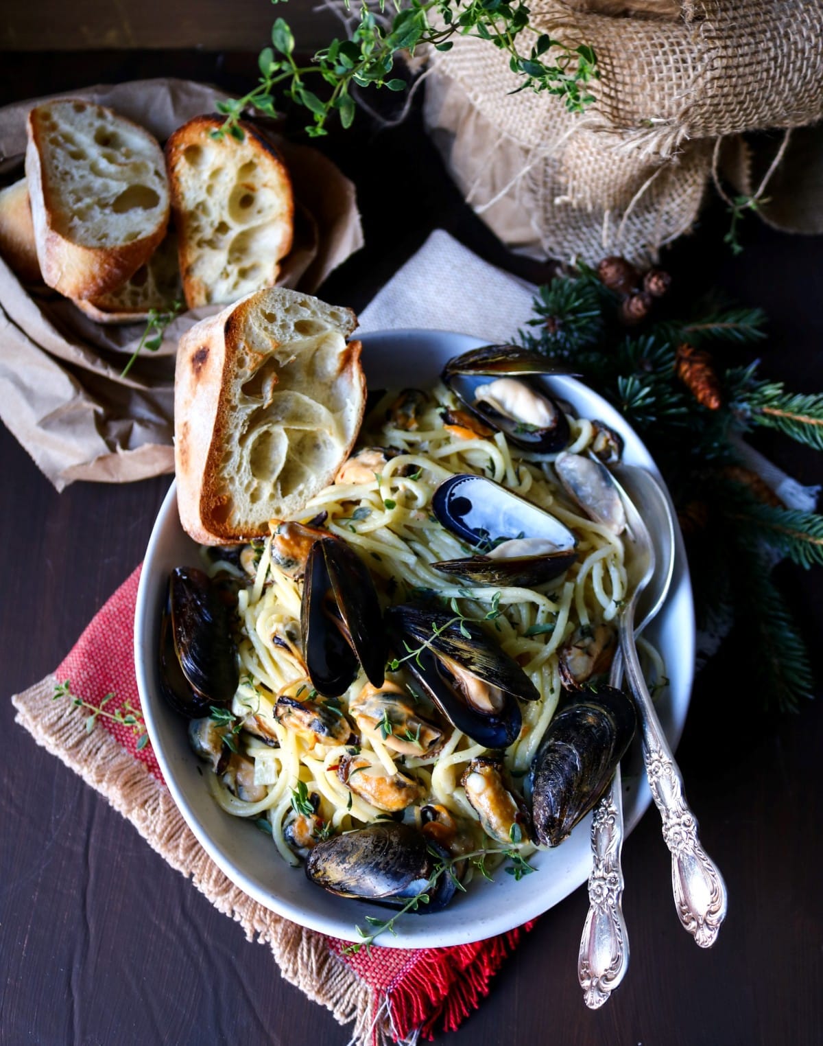 Garlic butter mussel pasta served in a white bowl with spaghetti, fresh thyme, and toasted bread on a dark wooden table.