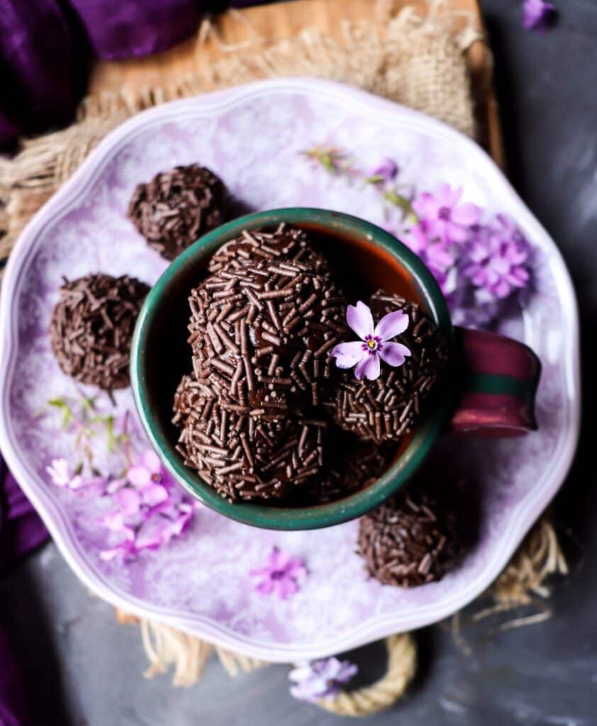 Brigadeiro chocolate fudge balls served in a purple cup, coated in chocolate sprinkles and garnished with small purple flowers.