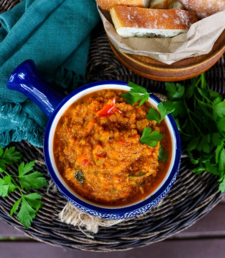 Bowl of zucchini caviar vegetable spread garnished with parsley, served with sliced rustic bread on a woven placemat with a dark wooden background.