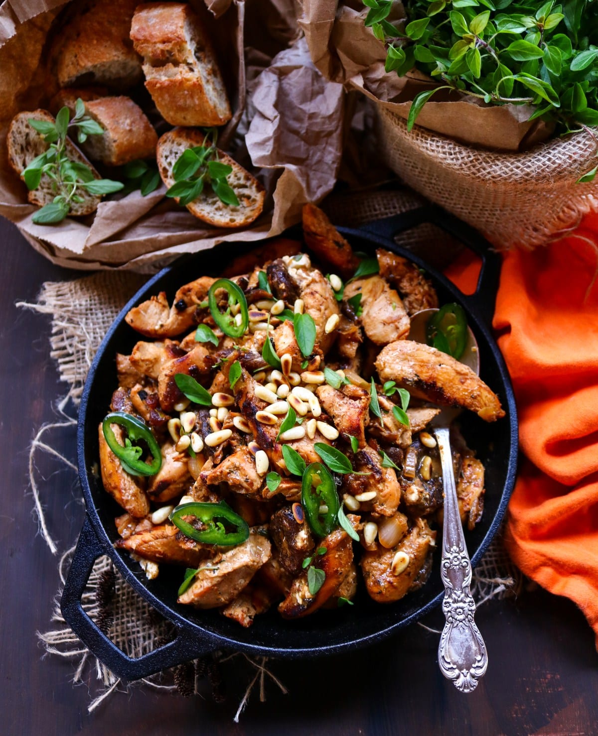 Apricot pine nut chicken skillet with toasted pine nuts, jalapeño slices, and herbs served in a cast iron pan.