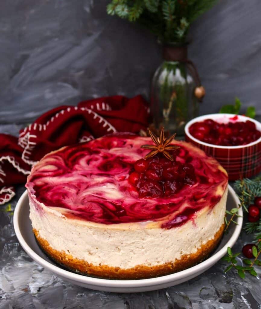 Whole spiced cranberry cheesecake with a cranberry swirl and holiday garnish on top.