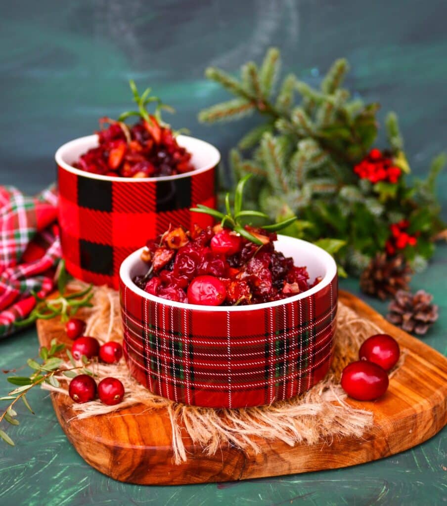Festive Cranberry Almond Relish with caramelized onions, rosemary, and honey served in plaid holiday bowls on a wooden board with fresh cranberries and pine branches — a vibrant red Christmas condiment perfect for holiday entertaining.