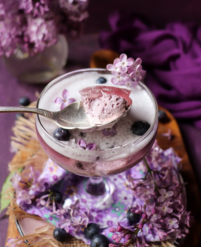 Creamy blueberry lilac panna cotta dessert with spoonful showing light, delicate texture.