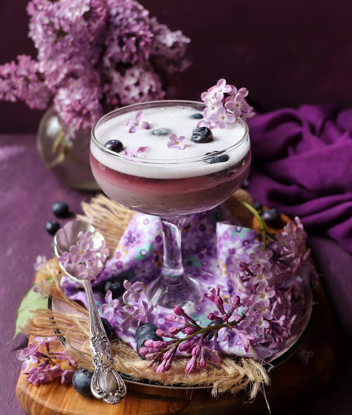 Blueberry lilac panna cotta styled with fresh blueberries and edible lilac flowers.