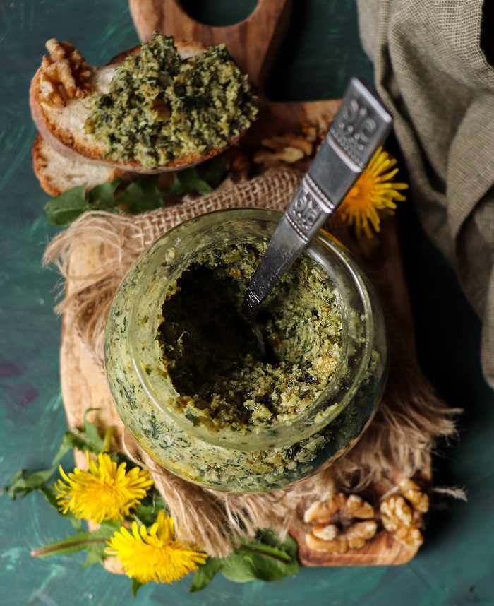 Dandelion greens pesto with walnuts served in a jar with spoon and spread on toasted bread.