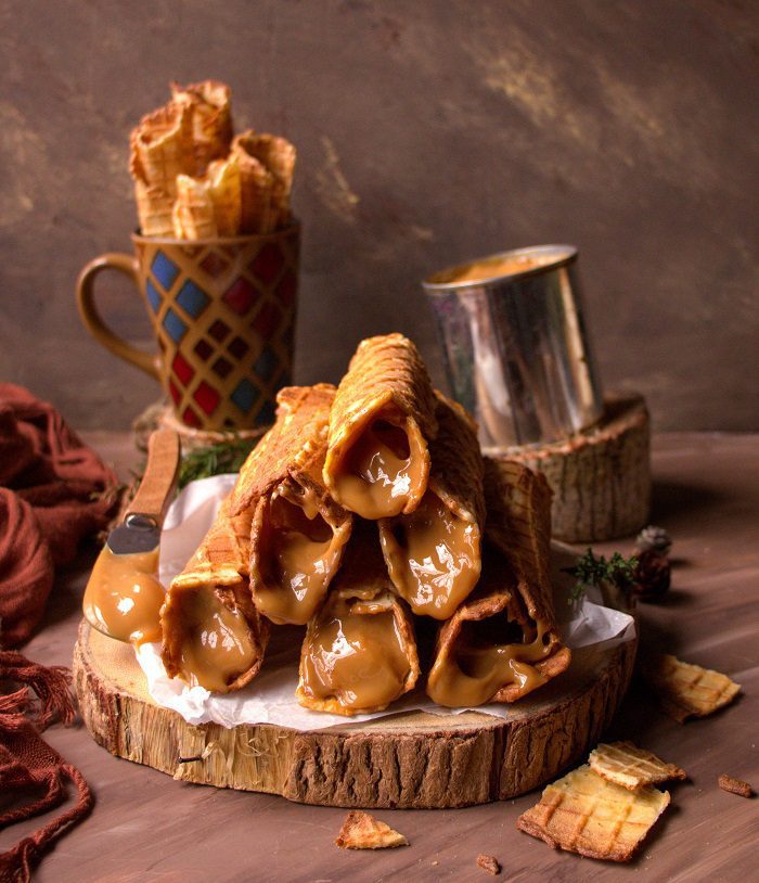Rolled waffle cookies filled with dulce de leche, stacked on a wooden board.