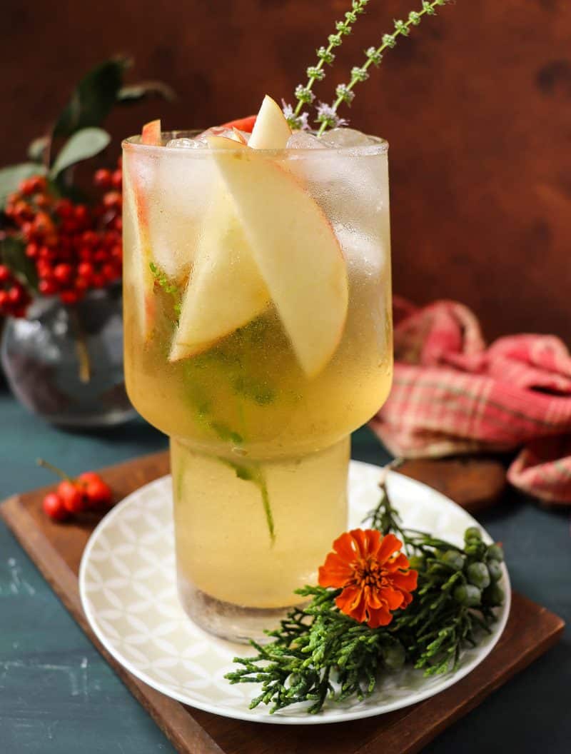 Apple cider rum cocktail with maple syrup, served over ice in a glass and garnished with cinnamon sticks and apple slices.