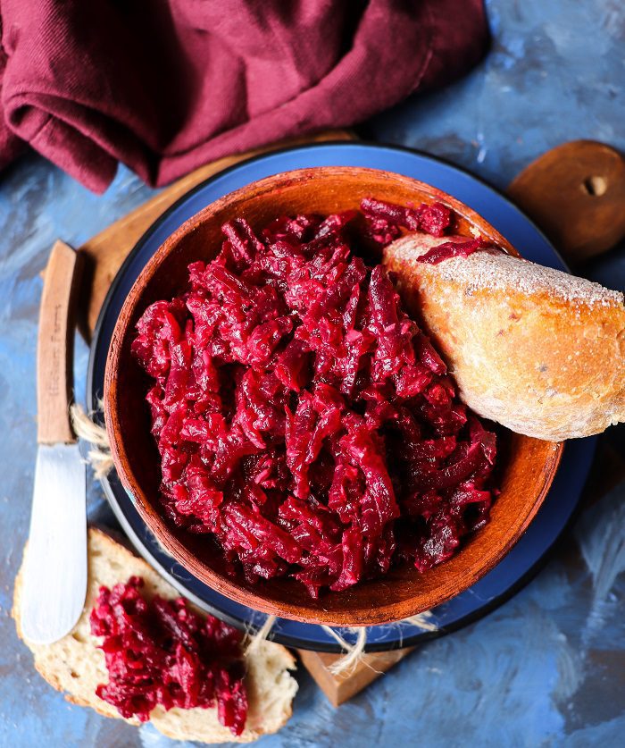 Beetroot horseradish dip made with grated beets, served in a rustic bowl with slices of bread on a dark, moody background.