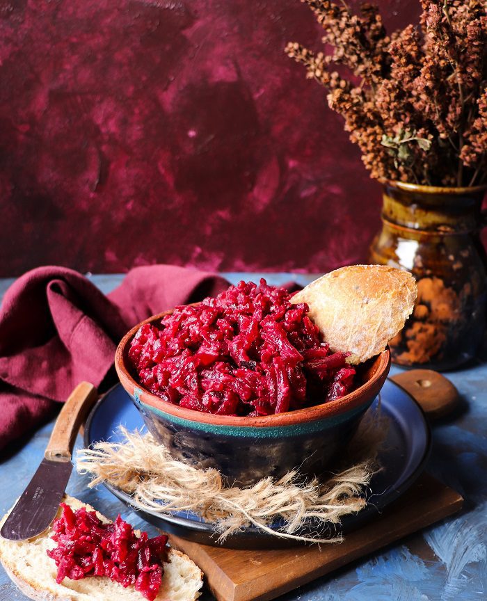 Beetroot horseradish dip made with grated beets, served in a rustic bowl with slices of bread on a dark, moody background.