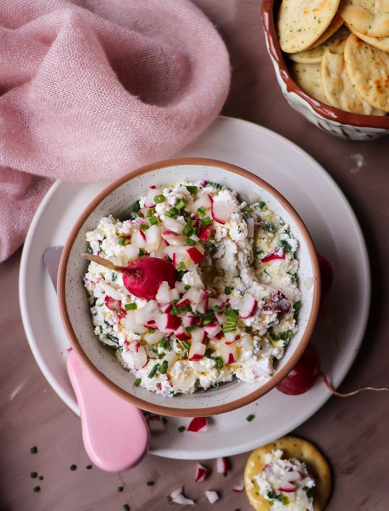 Rustic cottage cheese dip with radishes and chives in a bowl, topped with diced radishes and served with crackers on the side.