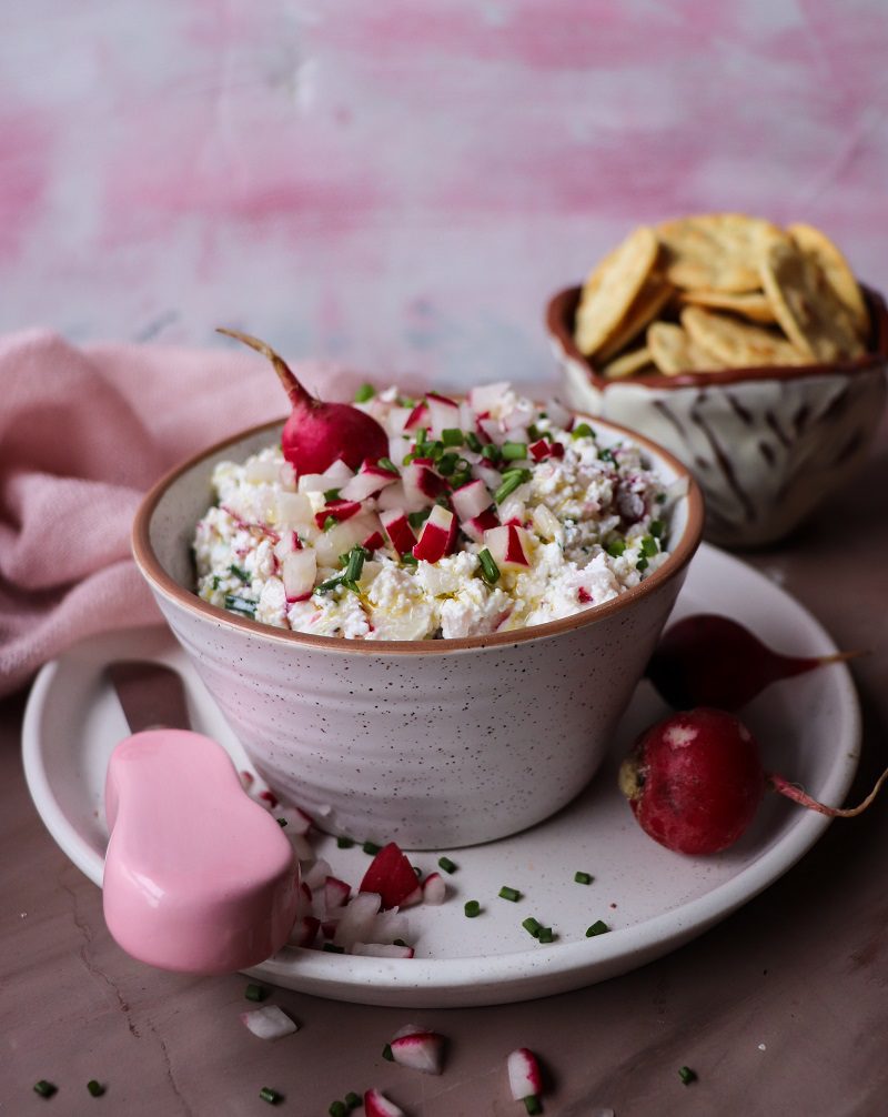 Rustic cottage cheese dip with radishes and chives in a bowl, topped with diced radishes and served with crackers on the side.
