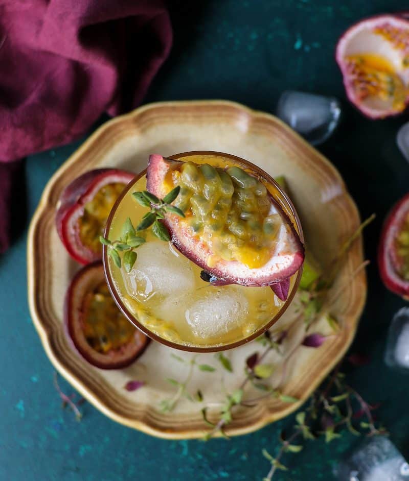 Overhead view of passion fruit green iced tea topped with fresh passion fruit pulp, thyme sprigs, and ice cubes.