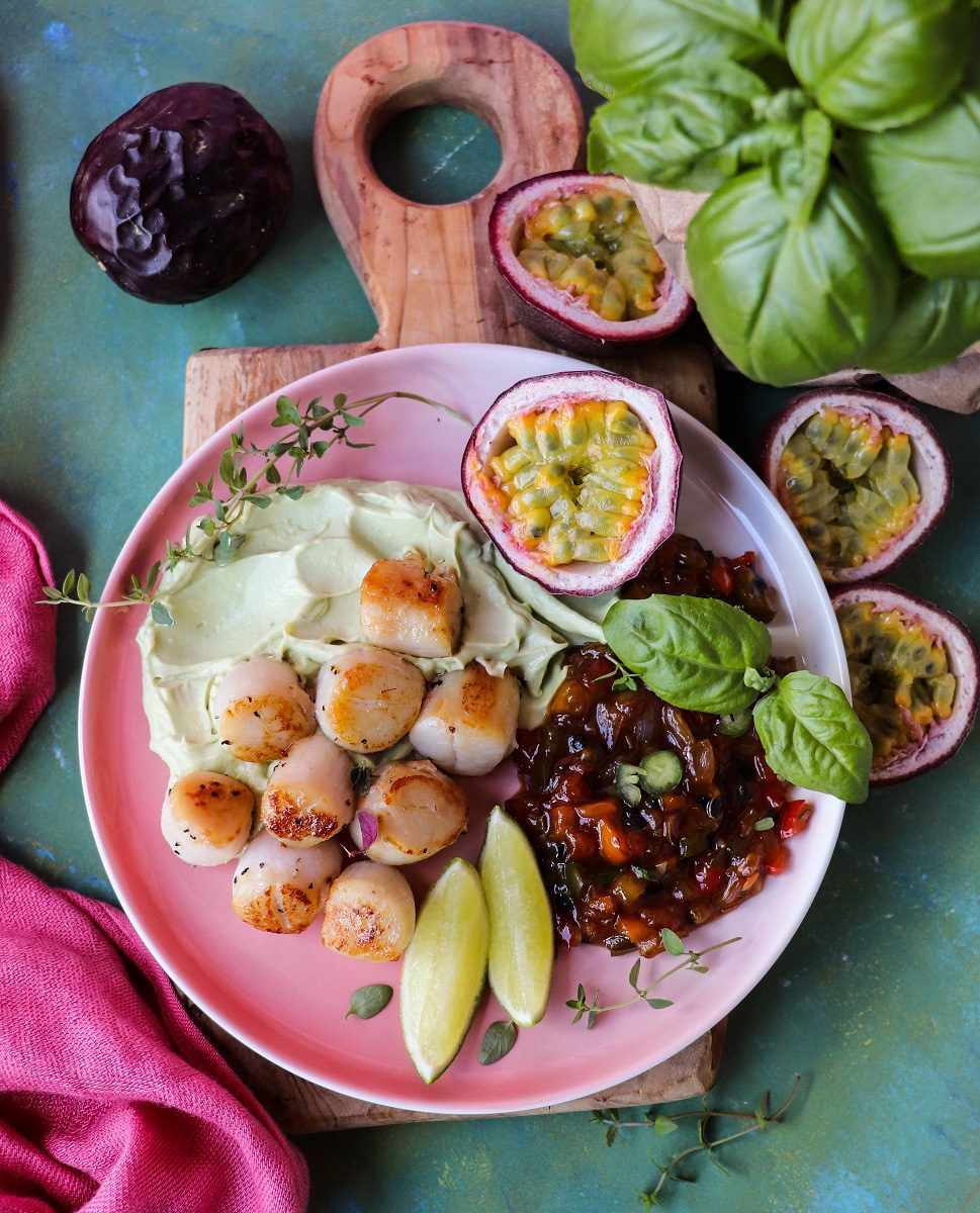 Seared scallops served with creamy avocado mousse and passion fruit sauce on a pink plate, an elegant and refined choice for romantic dinner recipes.