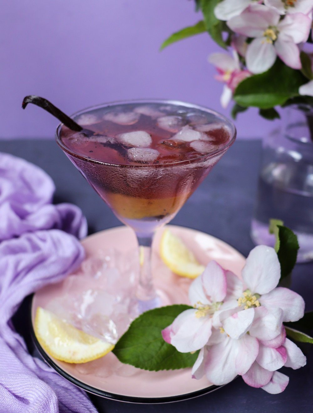 Vanilla Empress 1908 Gin Cocktail served in a chilled martini glass with ice, lemon peel, and delicate spring blossoms, styled on a soft lavender and pink setting.