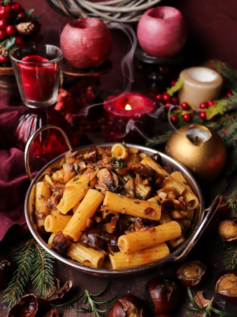 Plate of chestnut and prosciutto pasta with rosemary, golden onions, and chestnut pieces on a rustic table with fresh herbs.