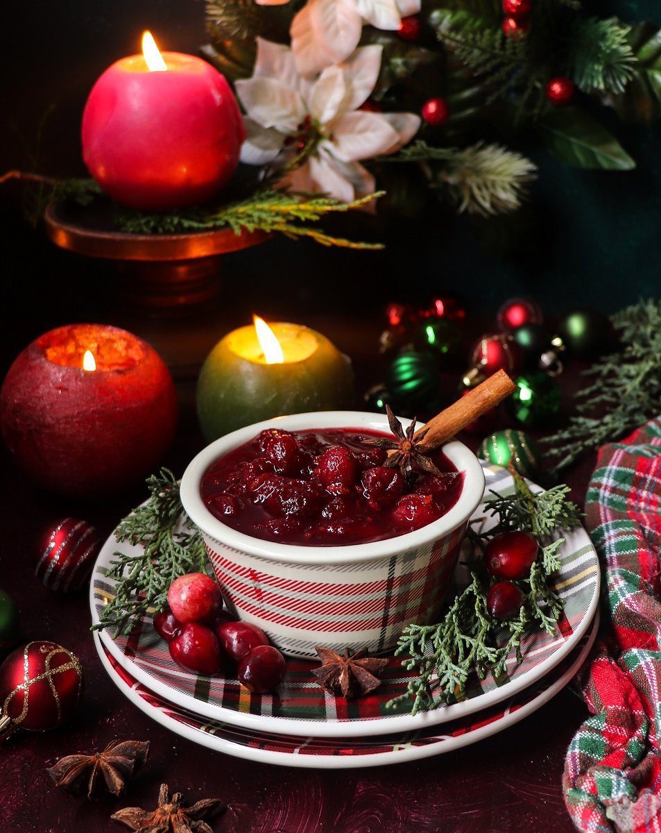 A bowl of festive rosé wine cranberry sauce garnished with star anise, cinnamon sticks, and fresh cranberries, surrounded by candles and holiday greenery.