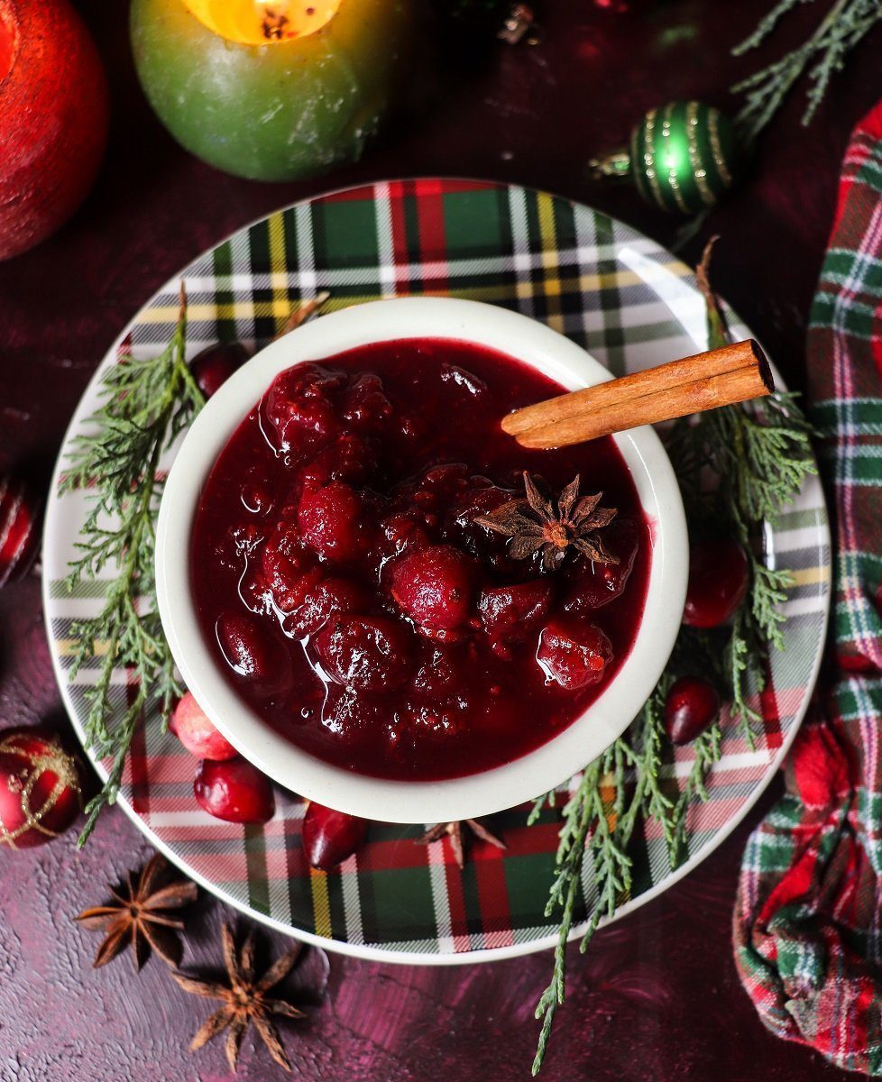 A bowl of rosé wine cranberry sauce topped with a cinnamon stick and star anise, set on a festive tartan plate with fresh cranberries and evergreen sprigs.