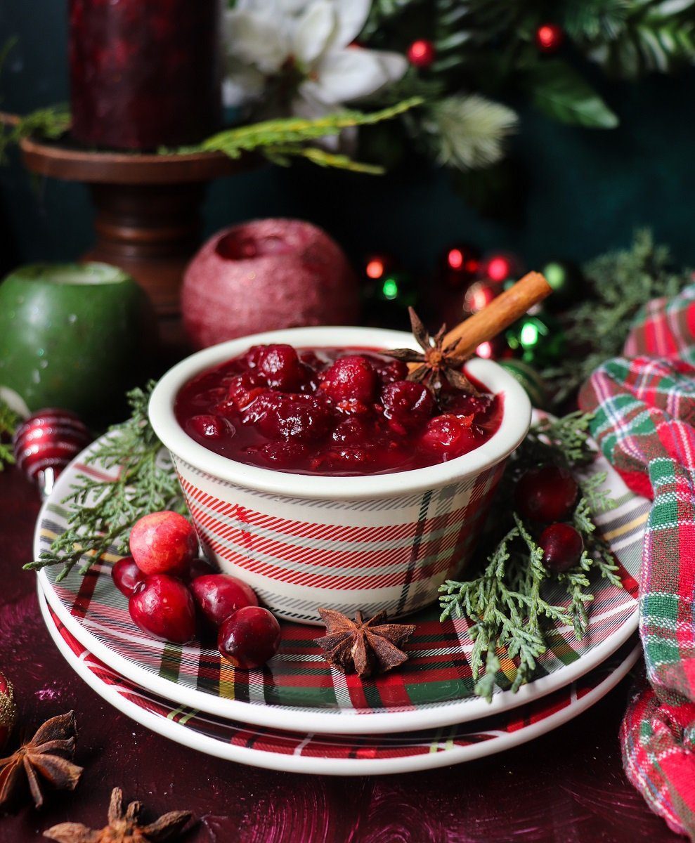 A bowl of festive rosé wine cranberry sauce garnished with star anise, cinnamon sticks, and fresh cranberries, surrounded by candles and holiday greenery.