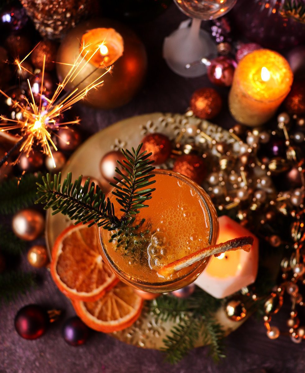 Festive Classic Mimosa Cocktail photographed from above with sparkling wine bubbles, orange garnish, Christmas ornaments, candles, and sparklers.