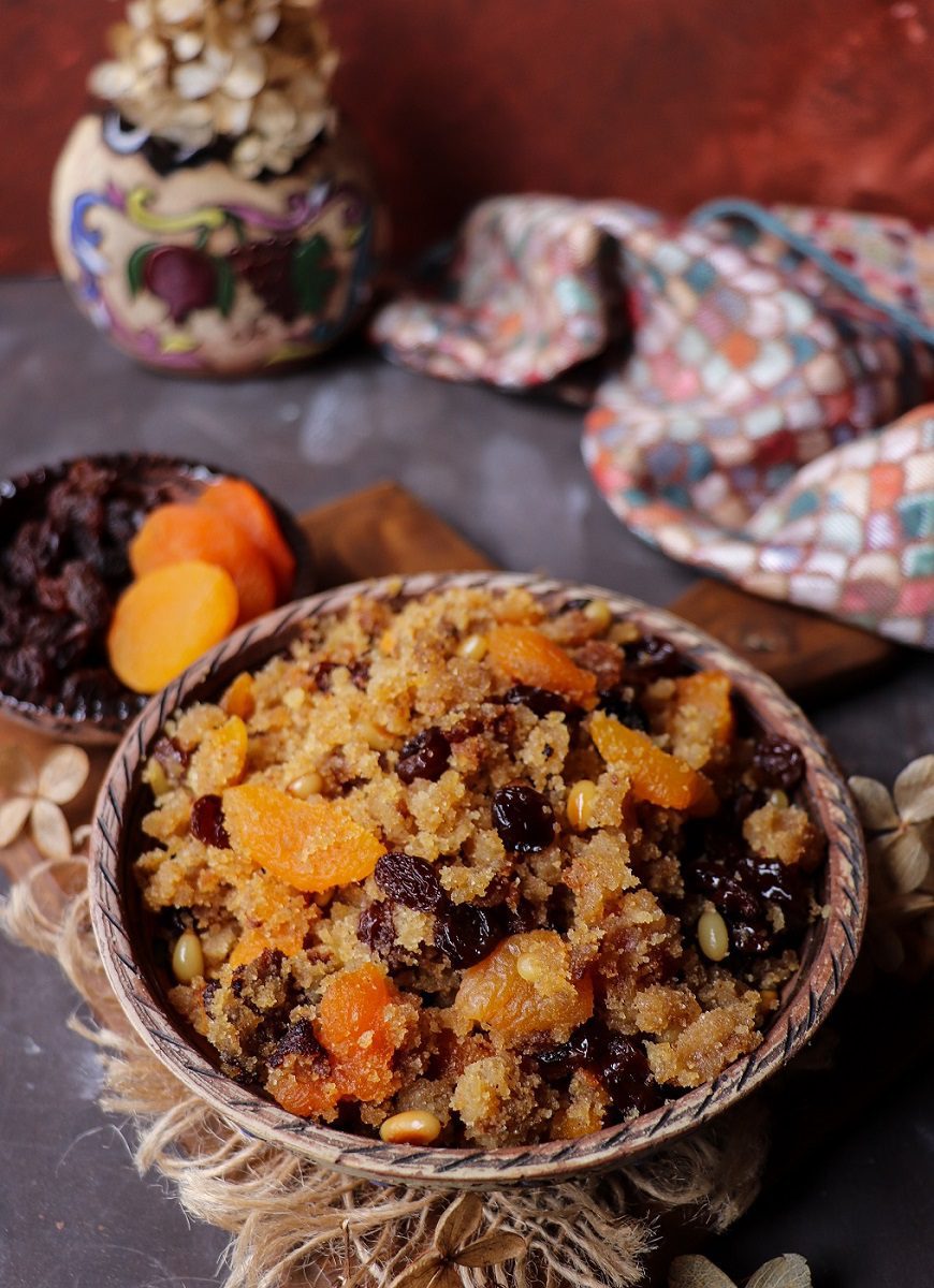 Semolina halwa (sooji halwa) with raisins, dried apricots, and pine nuts served in a decorative bowl with a spoon.