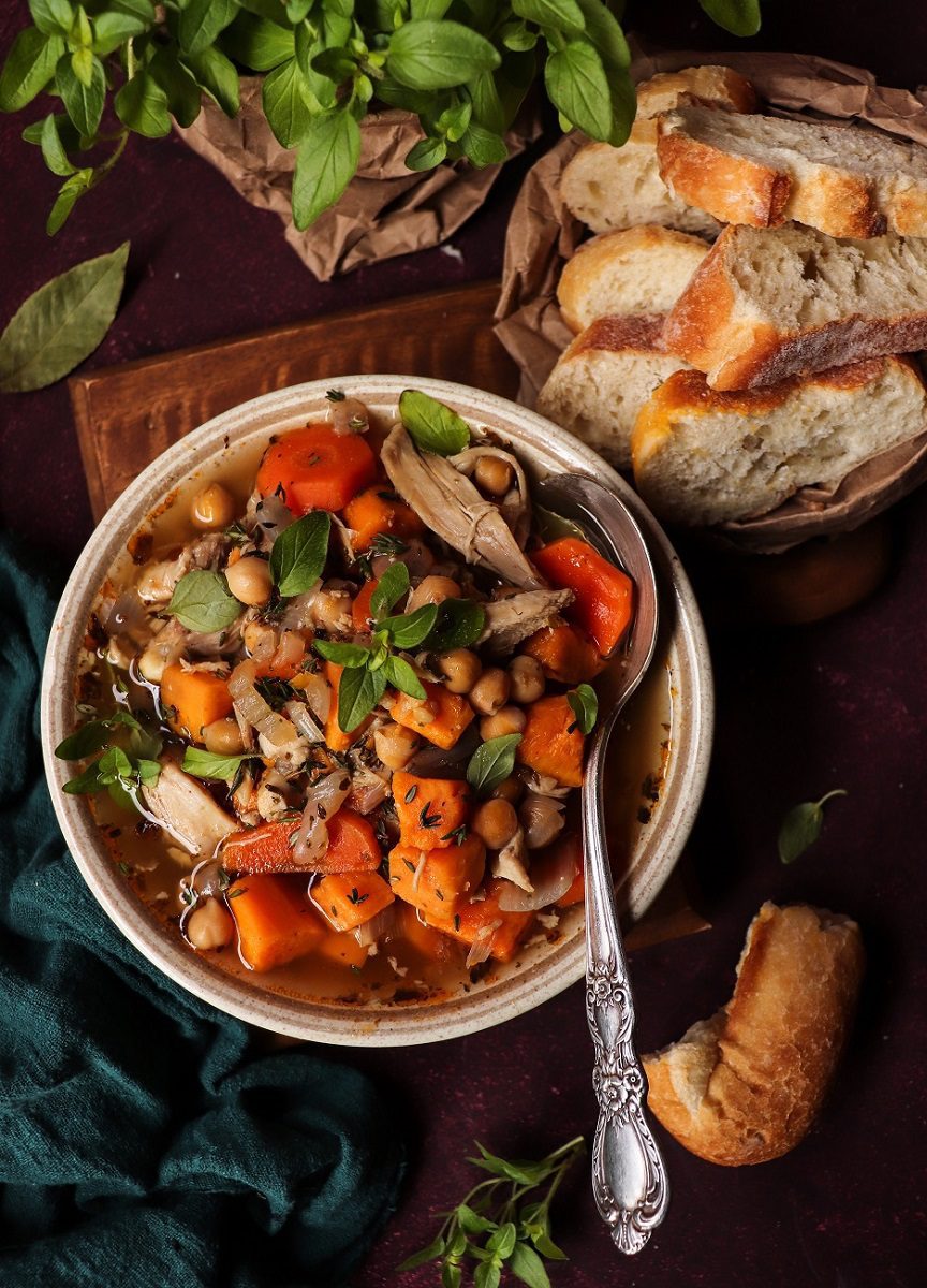 Chunky sweet potato chickpea soup with shredded chicken, carrots, onions, fresh herbs, and warm spices, served with crusty bread on the side.