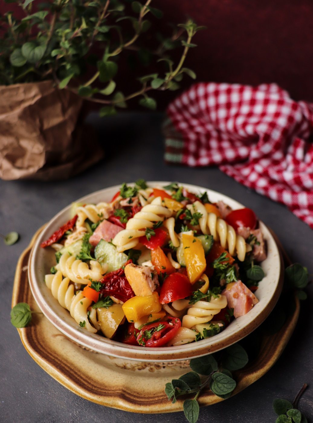 Mediterranean ham pasta salad with fusilli, cherry tomatoes, cucumber, sun-dried tomatoes, olives, fresh herbs, pine nuts, and shaved Parmesan, served with a light balsamic dressing.
