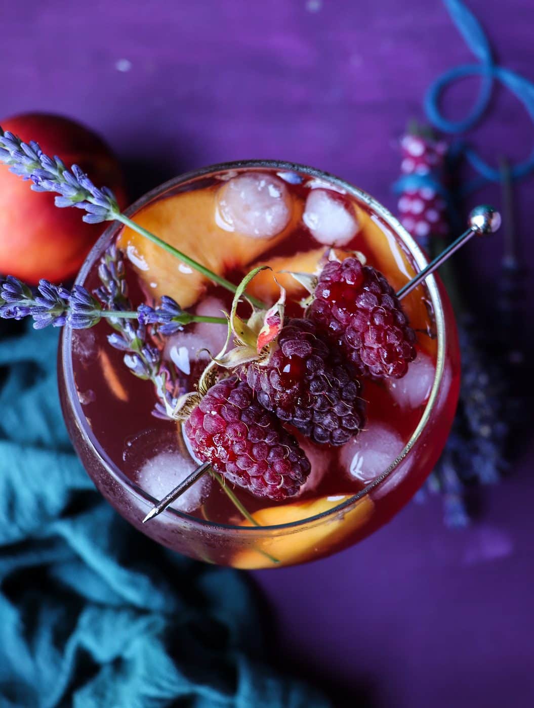 Peach raspberry sangria cocktail with lavender, ice cubes, and fresh fruit in a glass