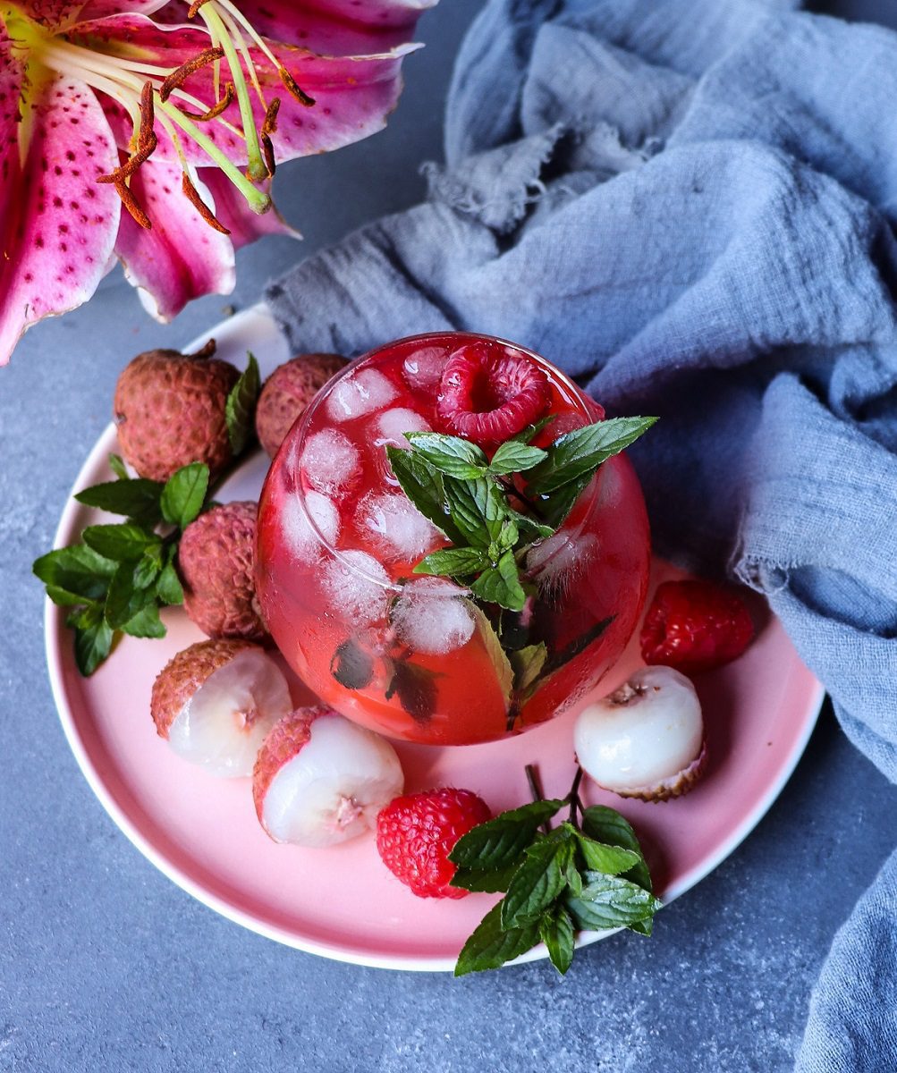 Rosé sangria with lychee and raspberries served over ice, garnished with fresh mint and raspberries.
