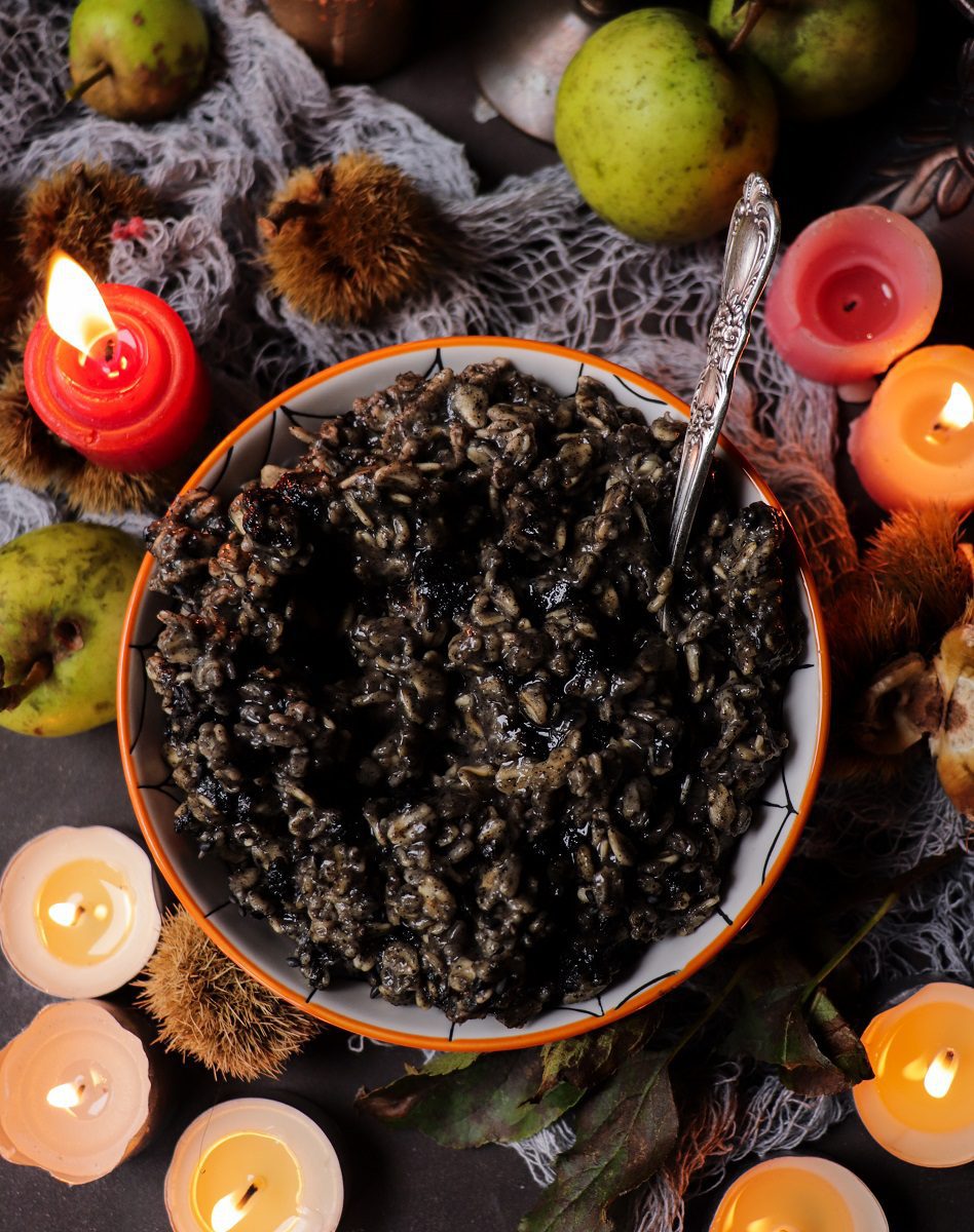 Black sesame seed oatmeal with a dark, creamy texture served in a bowl, styled with autumn decor and candles for a Halloween breakfast setting.