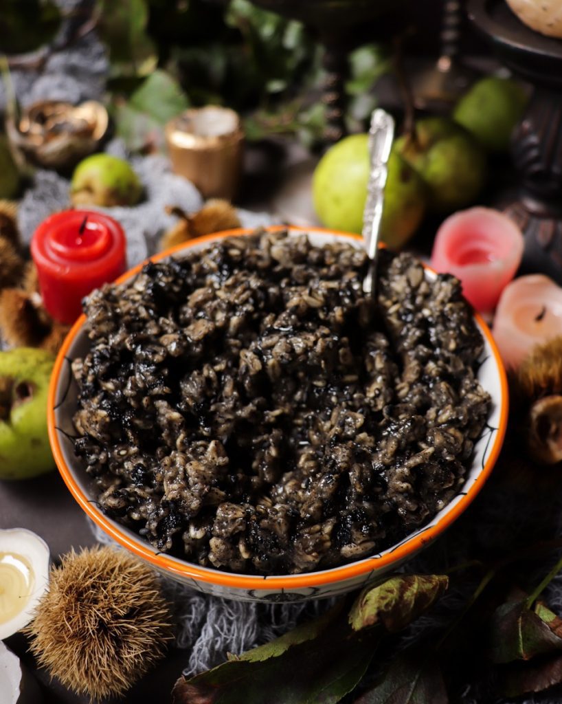 Black sesame seed oatmeal with a dark, creamy texture served in a bowl, styled with autumn decor and candles for a Halloween breakfast setting.