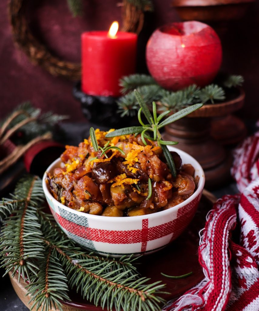 A festive bowl of Chestnut Pancetta Dip garnished with fresh rosemary and orange zest, set among evergreen branches and Christmas decorations for a cozy holiday presentation.