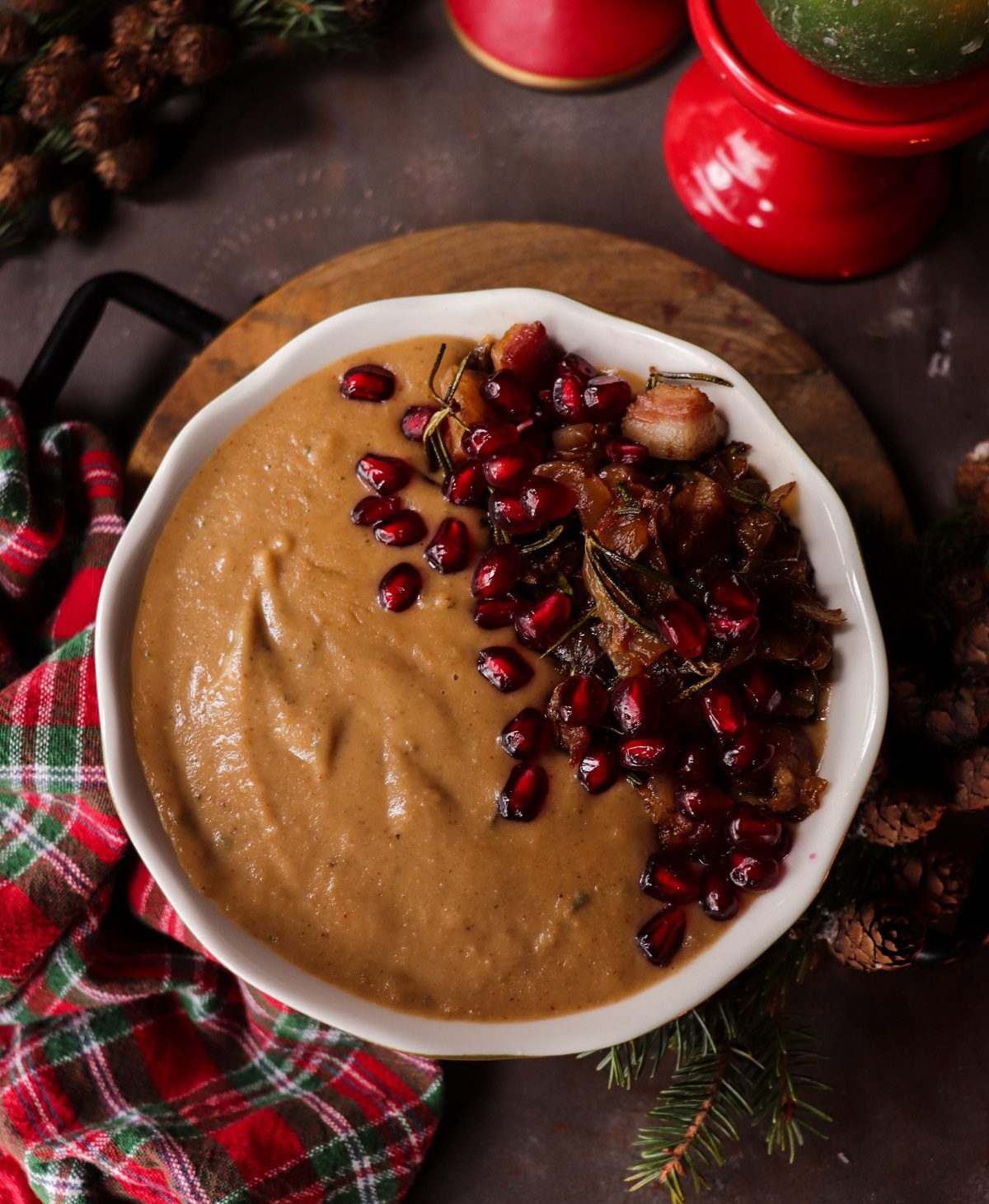 Creamy Chestnut Onion Soup topped with caramelized onions, crispy pancetta, and pomegranate arils in a festive bowl with winter candles and greenery.
