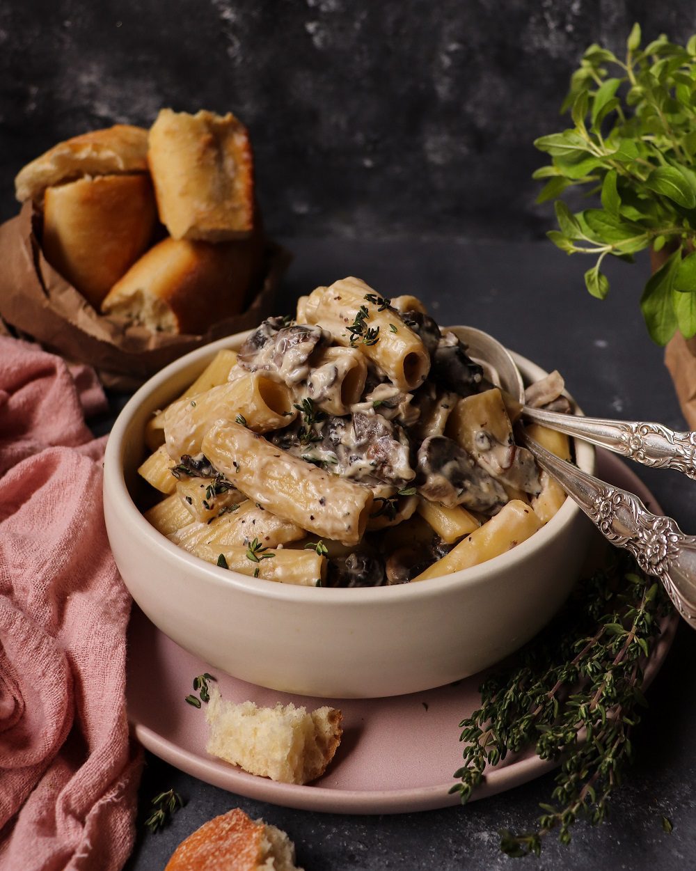 Creamy Mushroom Pasta made with browned mushrooms, garlic, thyme, and a silky cream cheese sauce coating short pasta, served in a bowl with fresh thyme, crusty bread, and herbs in the background.
