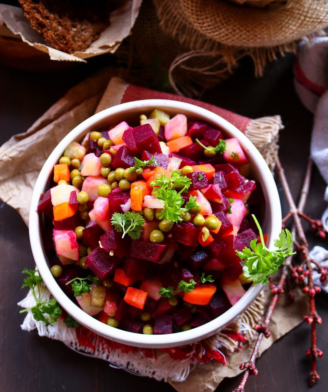 Beetroot Vinegret Salad with potatoes, carrots, peas and pickles served in a white bowl, garnished with parsley and styled with rustic rye bread.