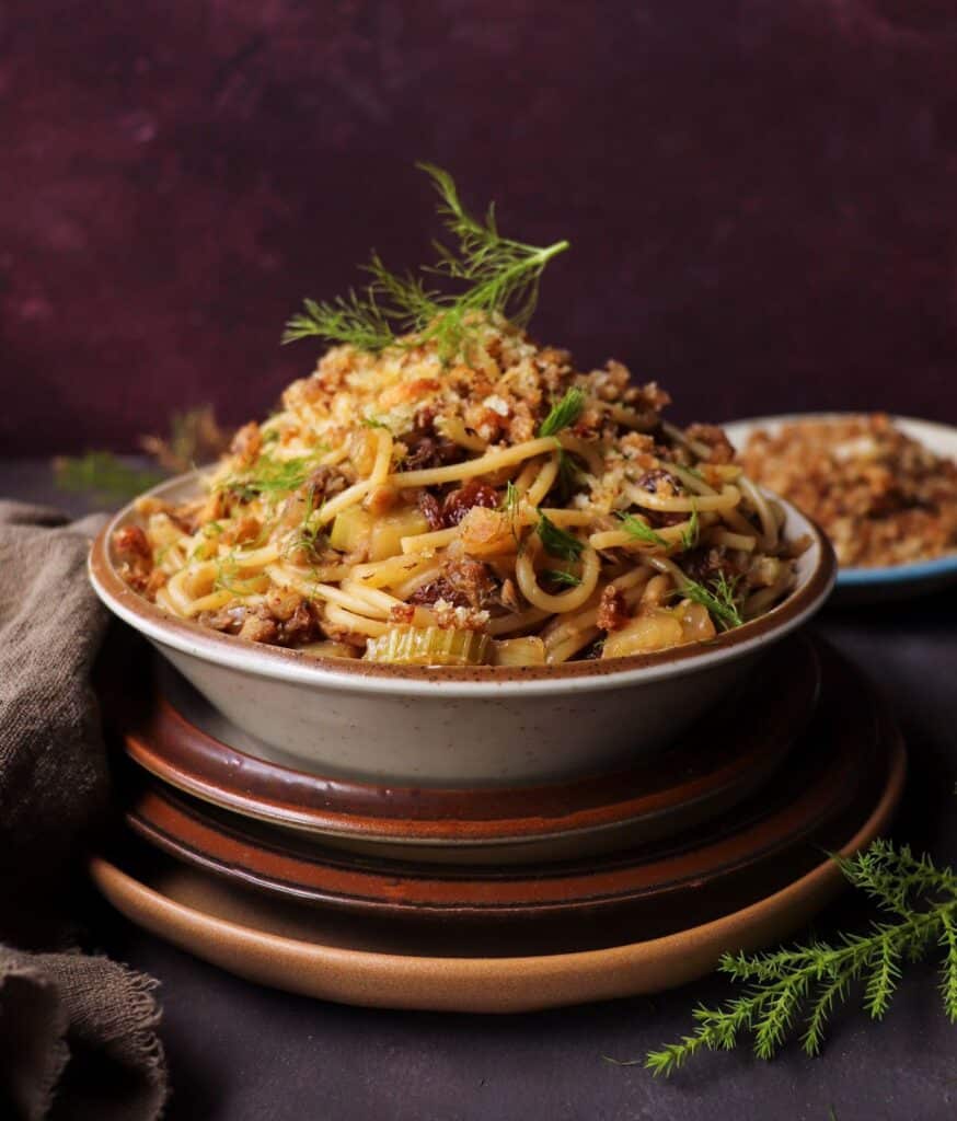 Sicilian pasta with sardines and fennel, topped with toasted breadcrumbs, raisins, and pine nuts, served in a rustic bowl.