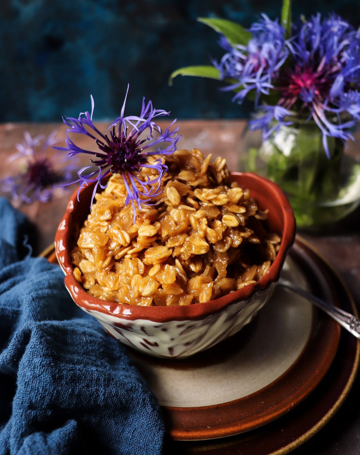 Creamy Irish cream oatmeal served in a rustic ceramic bowl, topped with shaved dark chocolate, styled as a rich dessert-style breakfast with purple flowers and a cozy, moody setting.