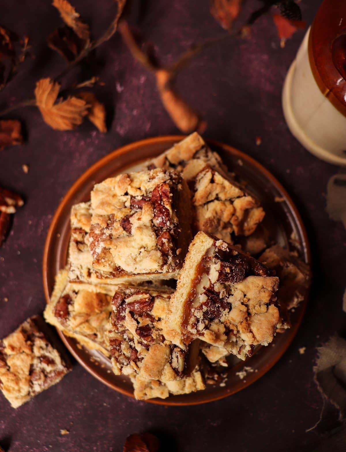 Stacked Dulce de Leche Shortbread Bars with thick caramel layer, chopped pecans, and golden crumb topping on a rustic plate.