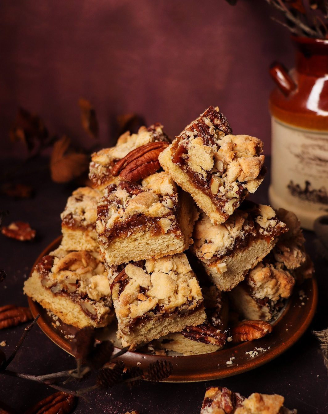 Stacked Dulce de Leche Shortbread Bars with thick caramel layer, chopped pecans, and golden crumb topping on a rustic plate.