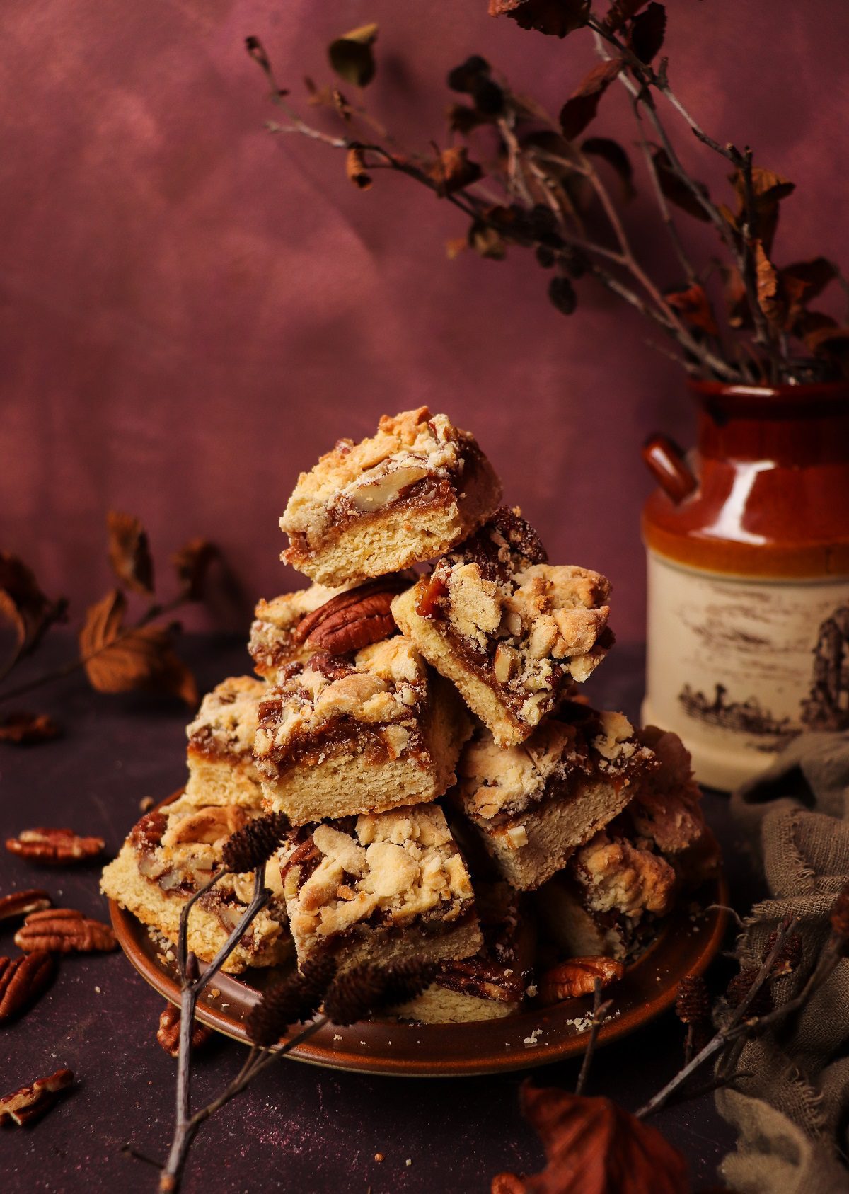 Stacked Dulce de Leche Shortbread Bars with thick caramel layer, chopped pecans, and golden crumb topping on a rustic plate.