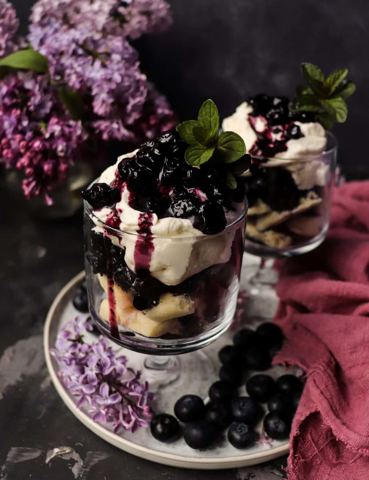 Blueberry Trifle with Lilac Infused Cream layered with shortbread cookies, blueberry sauce, whipped cream, fresh lilac blossoms, and mint.