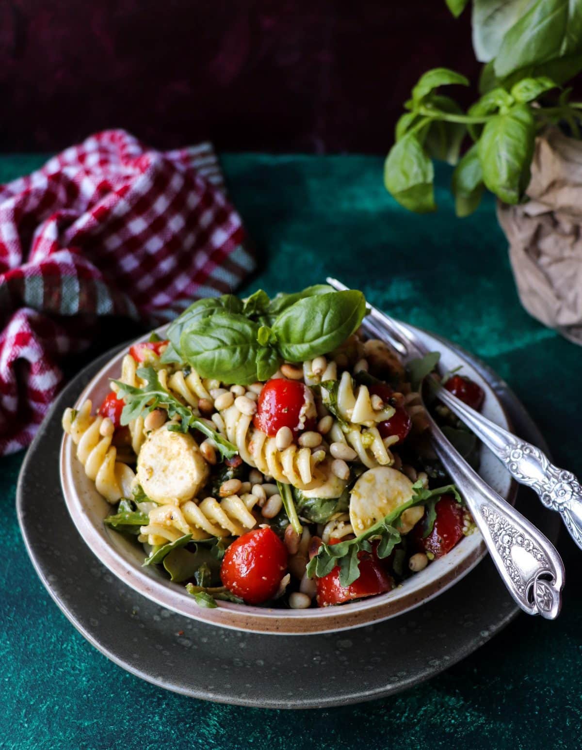 Pesto pasta salad with mozzarella, cherry tomatoes and toasted pine nuts in a bowl, garnished with fresh basil leaves.