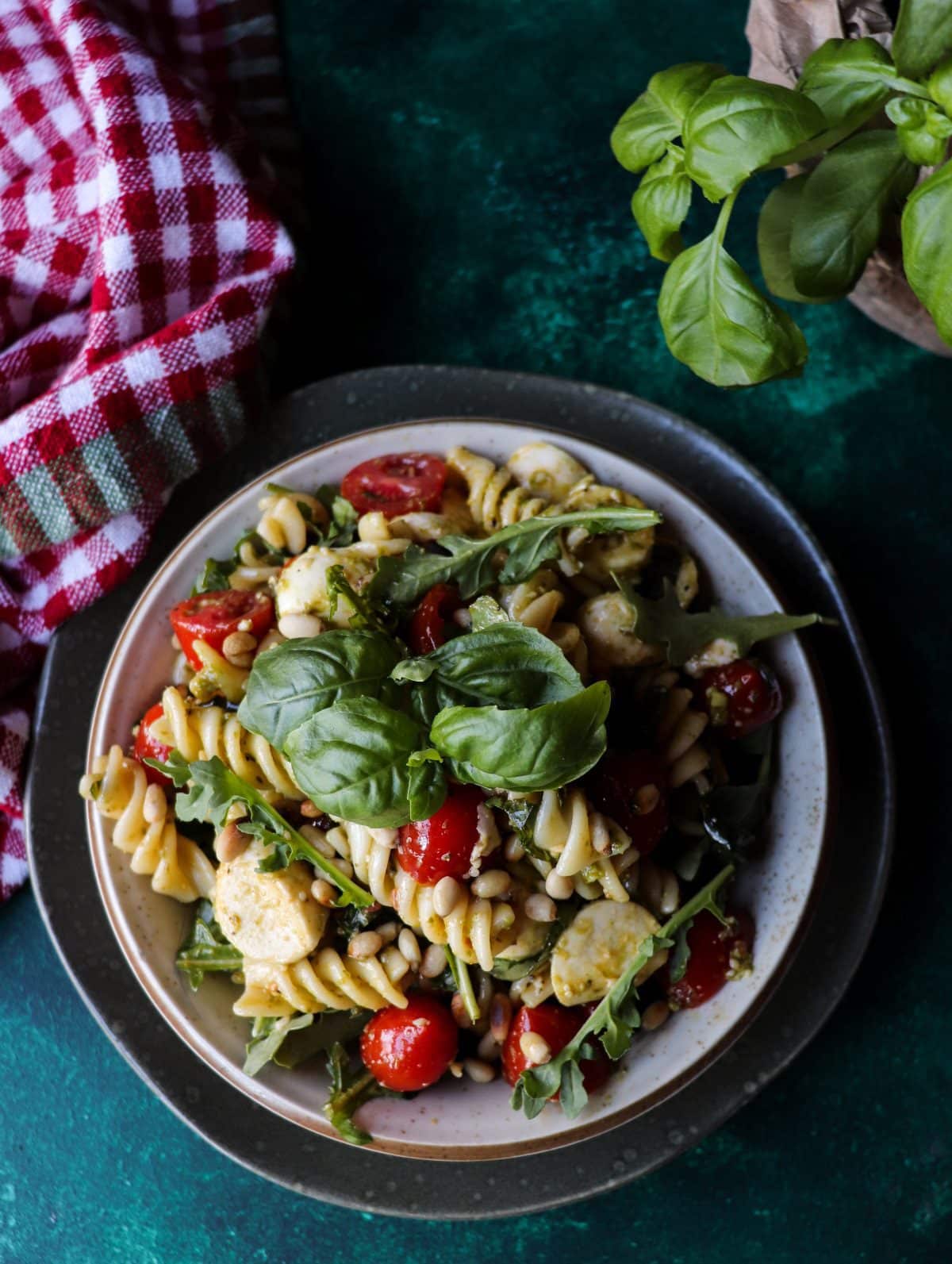 Pesto pasta salad with mozzarella, cherry tomatoes and toasted pine nuts in a bowl, garnished with fresh basil leaves.