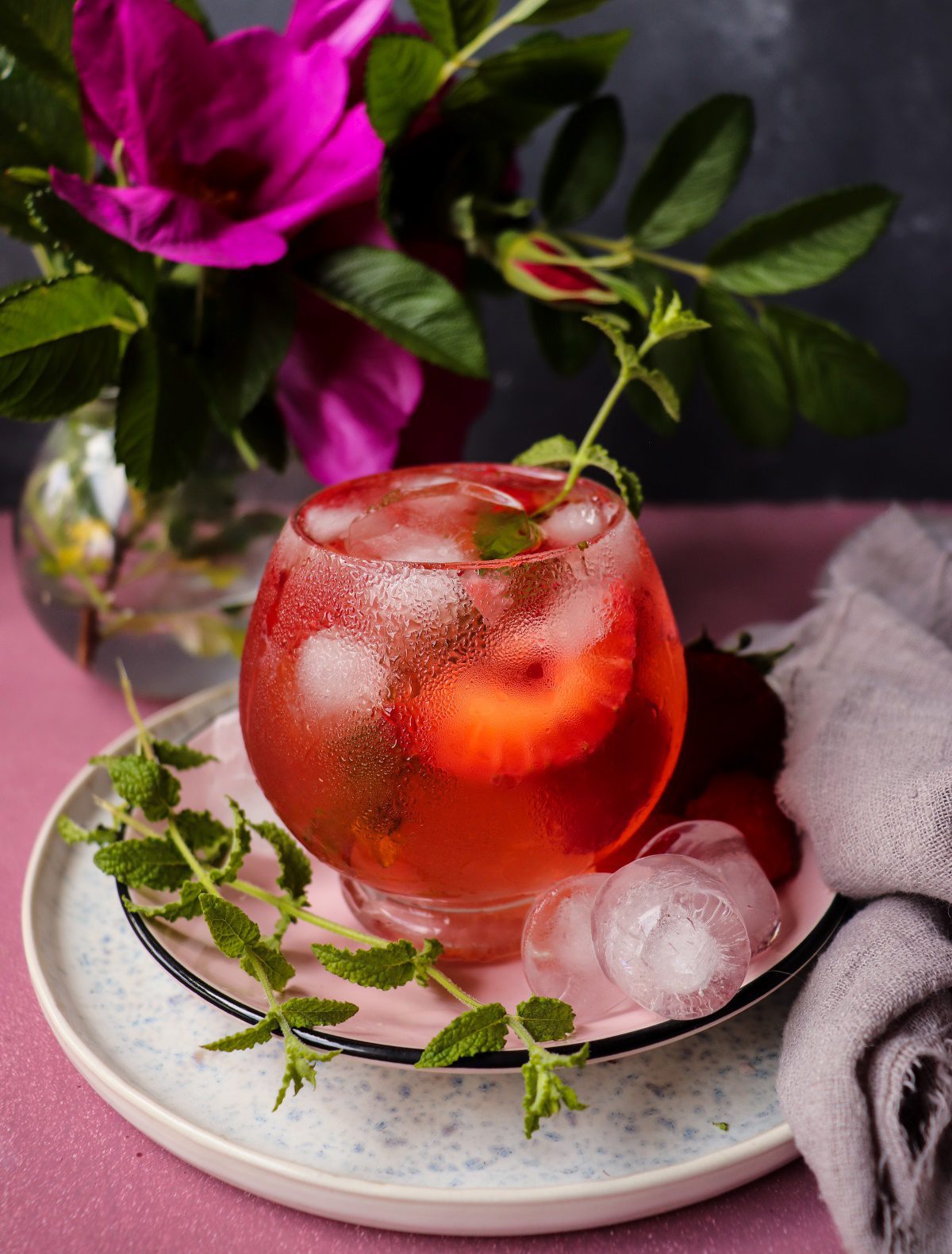 Rosé sangria served over ice with fresh raspberries and mint, showing a light pink floral cocktail.