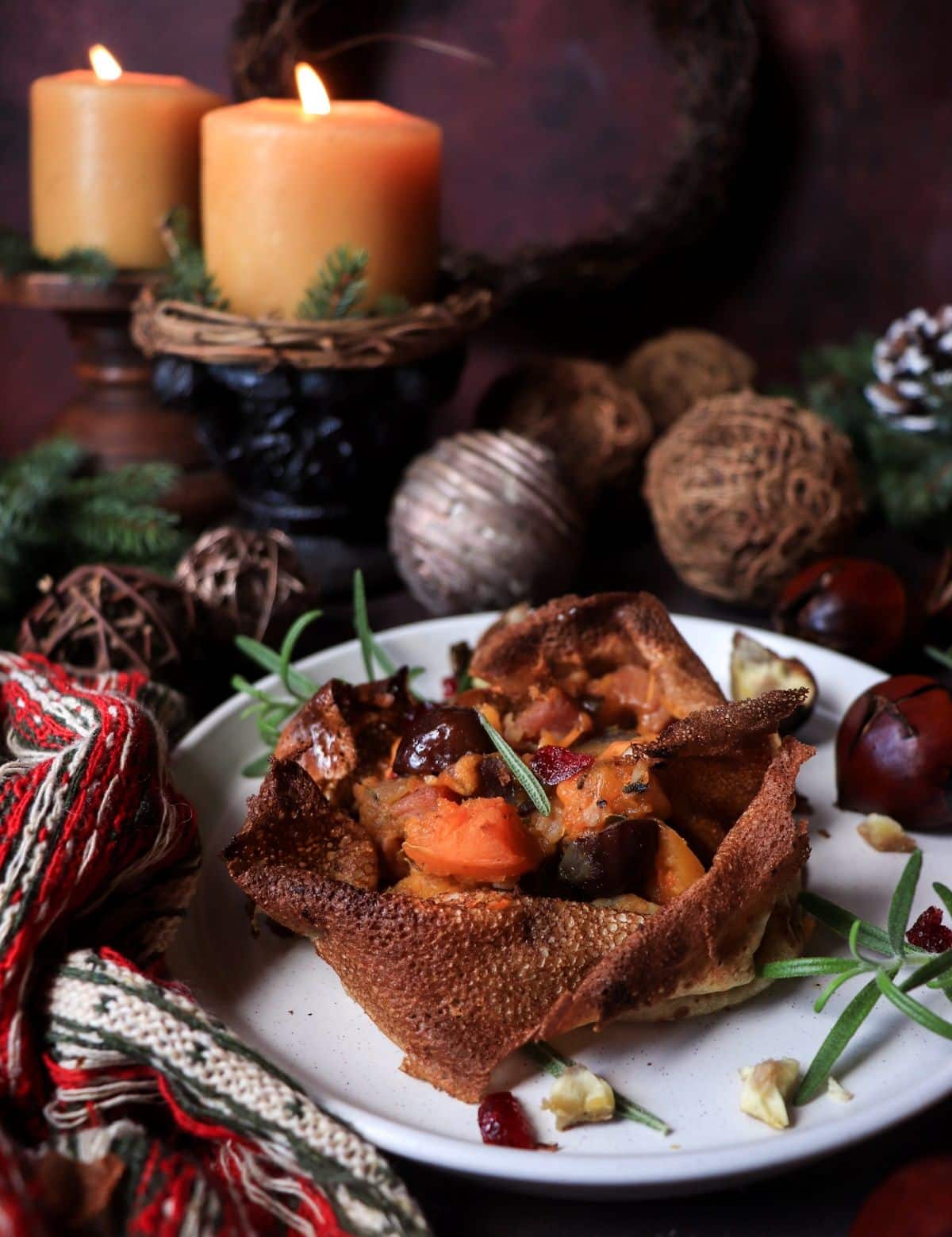 Crêpe bowl filled with roasted butternut squash, chestnuts, ham, prosciutto, and cranberries, garnished with rosemary and surrounded by festive winter décor